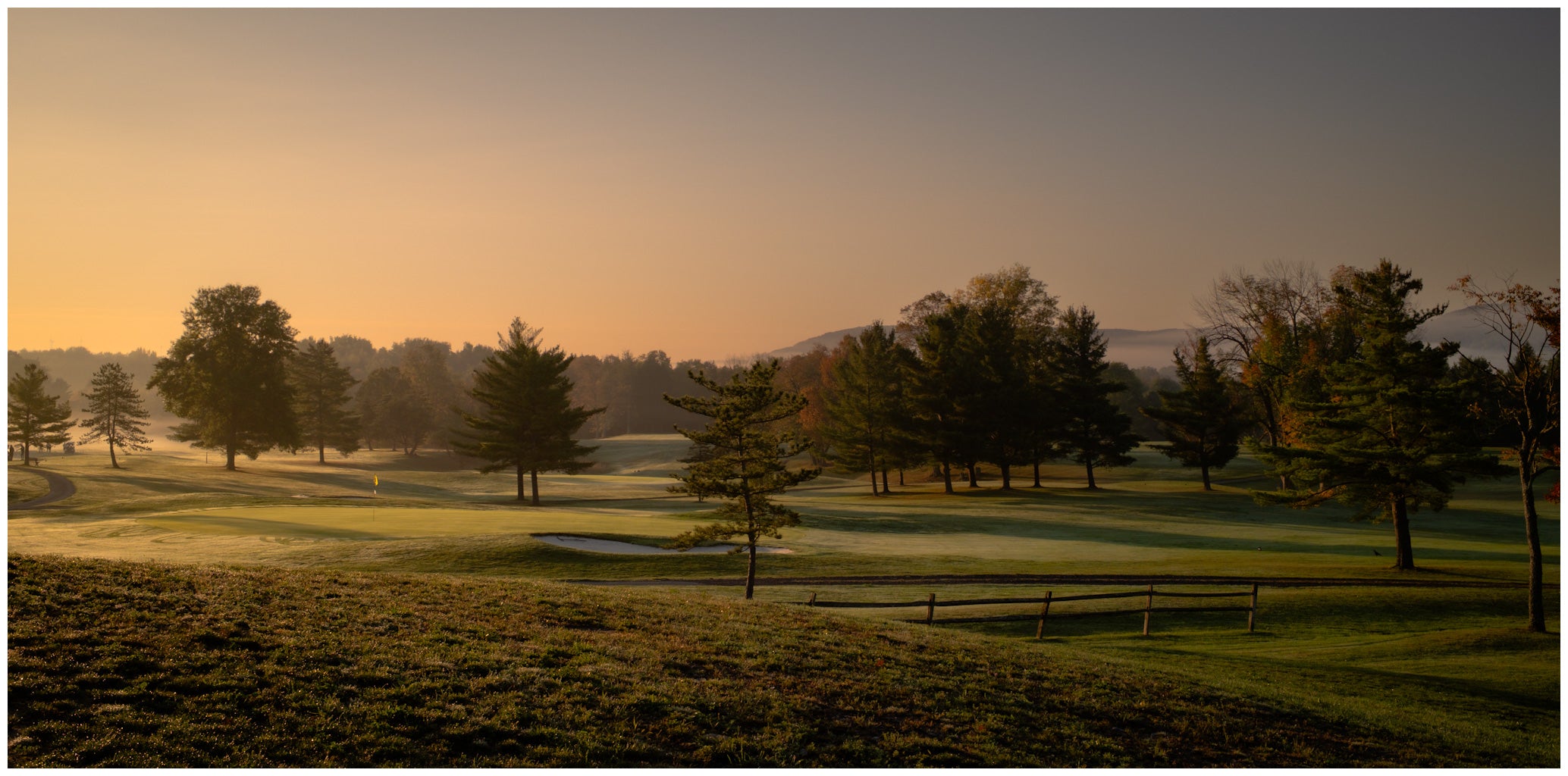 Golf course at sunrise with trees and a fence in the foreground